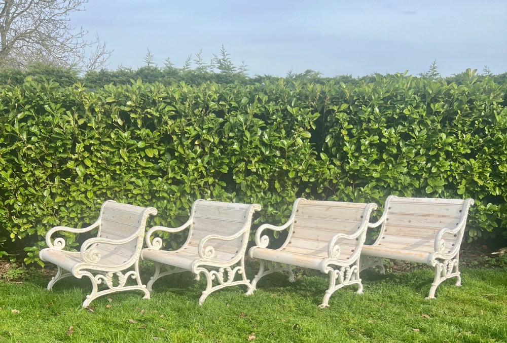 Set of four Victorian garden armchairs featuring white painted cast iron scrollwork frames and slatted timber seats.