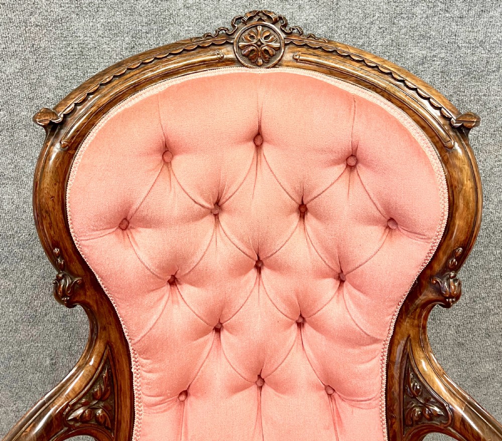 A Victorian open armchair crafted from carved dark walnut with button-backed rose pink velvet upholstery and brass castors. View IV