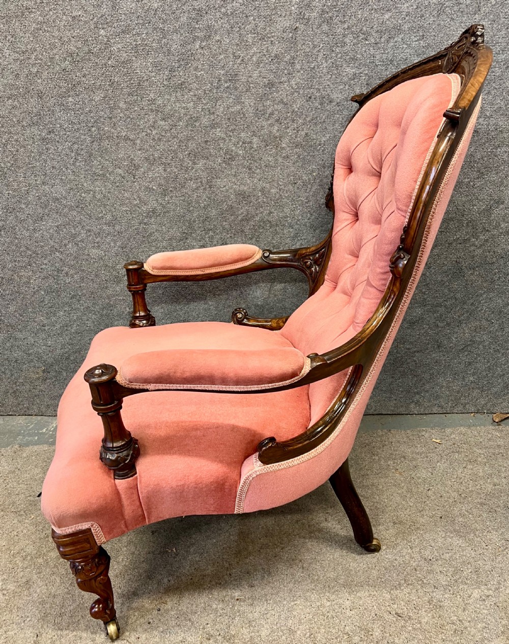 A Victorian open armchair crafted from carved dark walnut with button-backed rose pink velvet upholstery and brass castors. View VIII