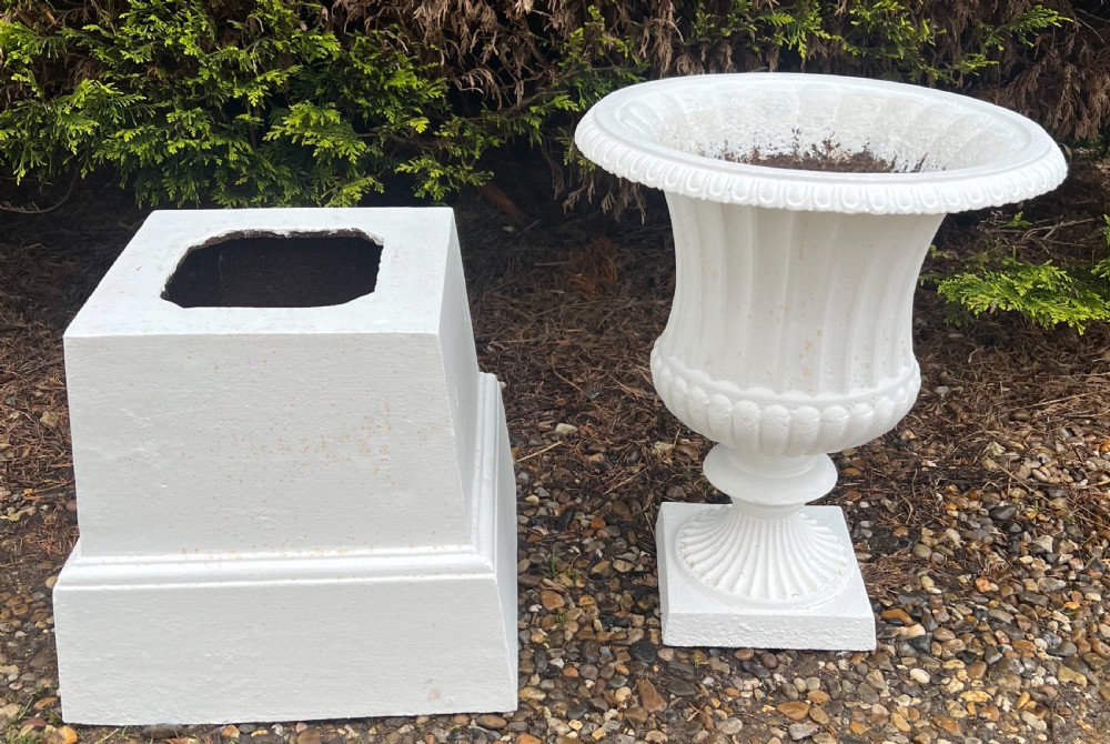 A white painted 19th-century cast iron garden urn featuring a fluted body atop a matching stepped pedestal stand. View VI