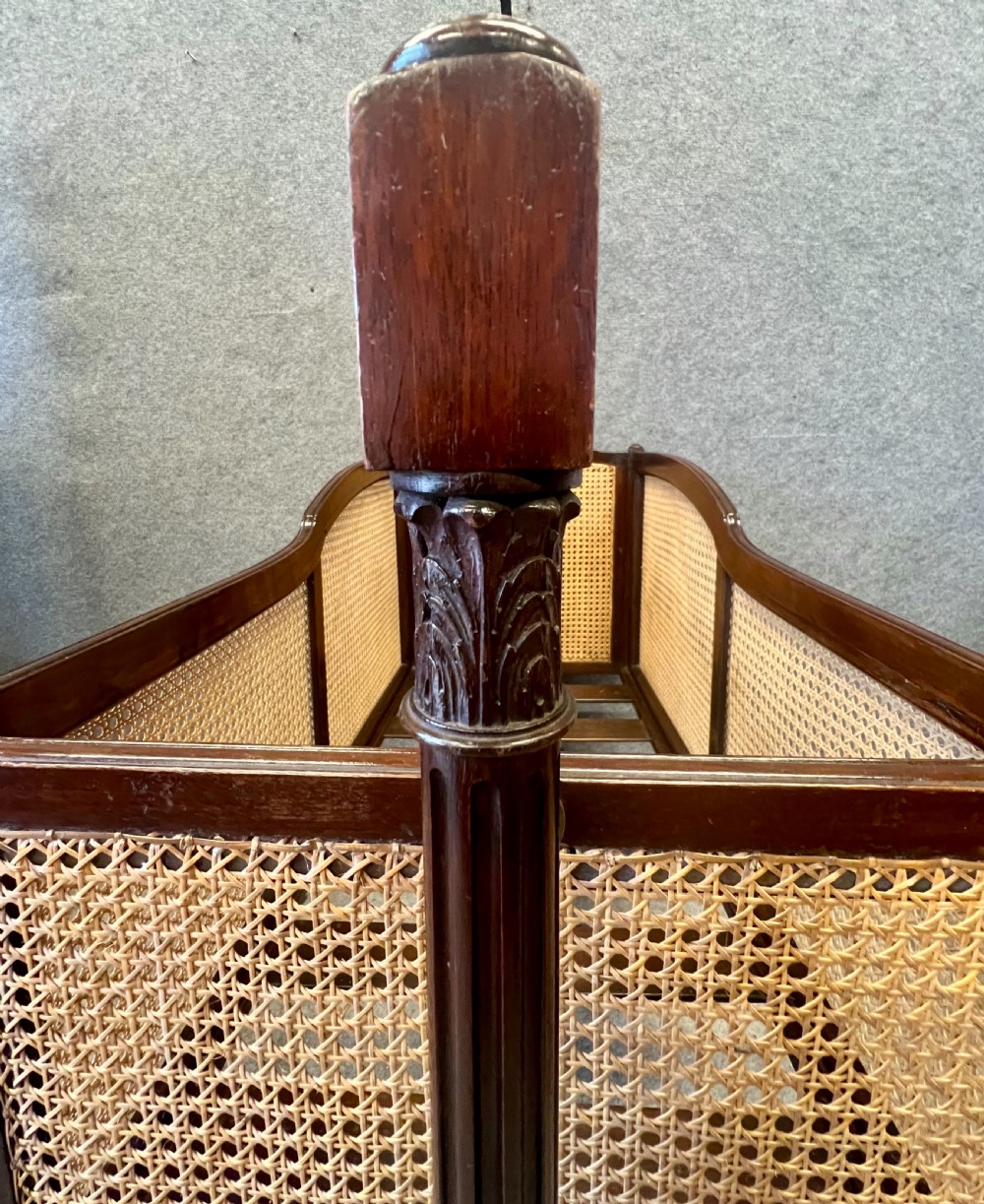 An antique Edwardian dark mahogany swinging crib with woven cane side panels and a lace drape suspended from a tall wooden pole. View VI