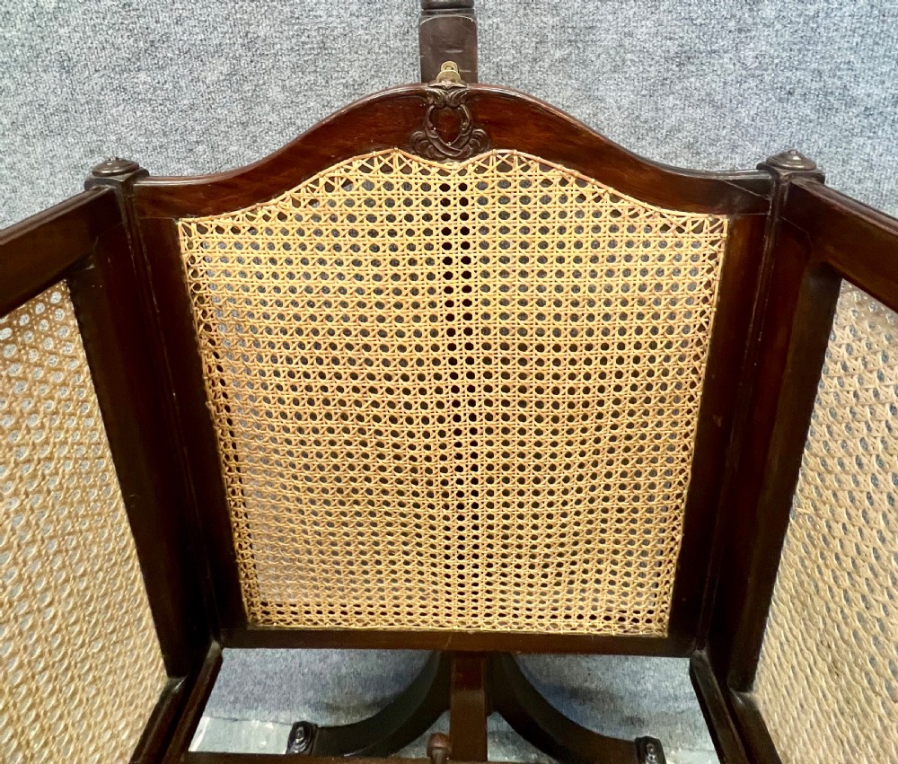 An antique Edwardian dark mahogany swinging crib with woven cane side panels and a lace drape suspended from a tall wooden pole. View VII