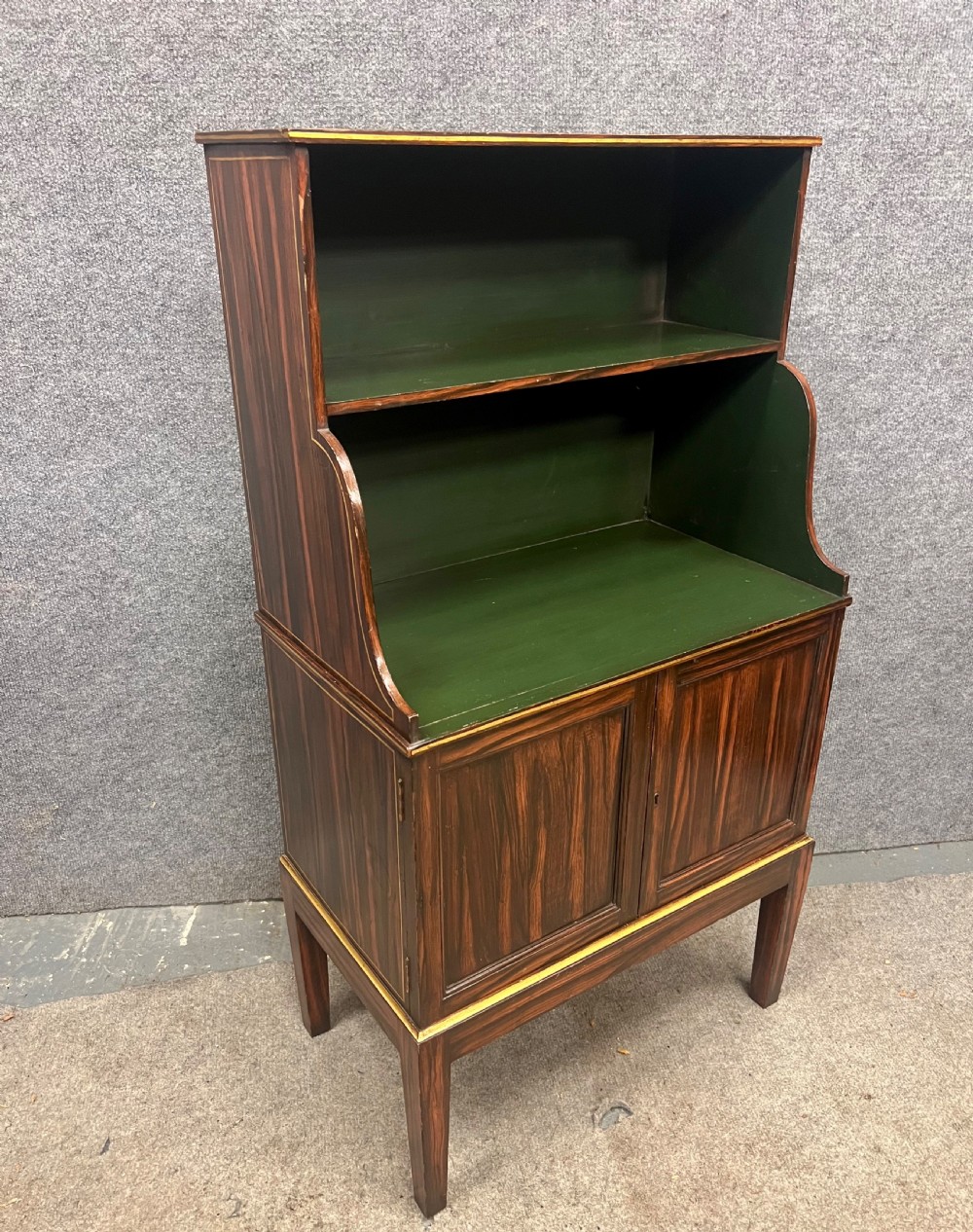 A Regency style dark wood waterfall bookcase featuring two open green-painted shelves over a double-door lower cabinet on tapered legs.
