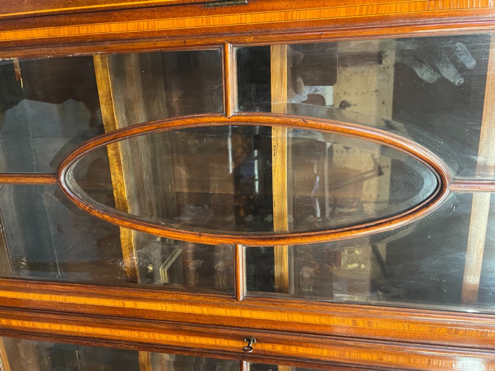 An Edwardian mahogany glazed bookcase with satinwood crossbanding, oval astragal door glazing, two drawers, and a double-door lower cupboard. View V