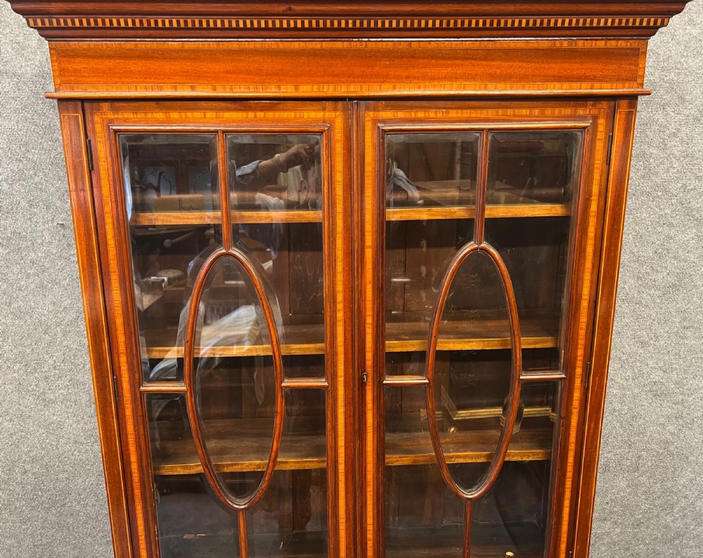 An Edwardian mahogany glazed bookcase with satinwood crossbanding, oval astragal door glazing, two drawers, and a double-door lower cupboard. View VII