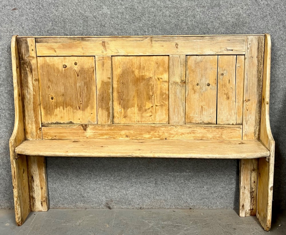 An antique light pine wooden settle featuring a high three-panel backrest, flat plank seat, and solid shaped side supports.
