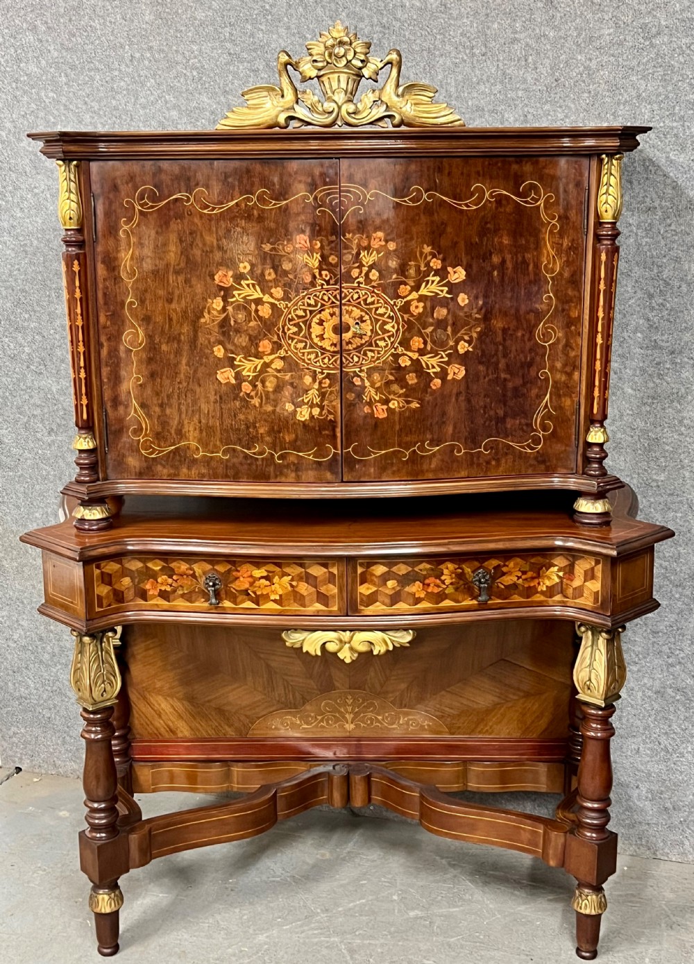 A two-tier dark walnut cocktail cabinet featuring intricate floral marquetry, a serpentine front, gilded carved accents, and turned legs with a contoured stretcher. View II