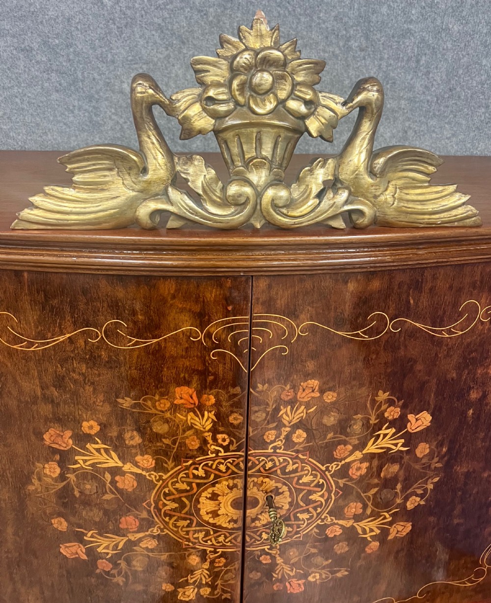A two-tier dark walnut cocktail cabinet featuring intricate floral marquetry, a serpentine front, gilded carved accents, and turned legs with a contoured stretcher. View V