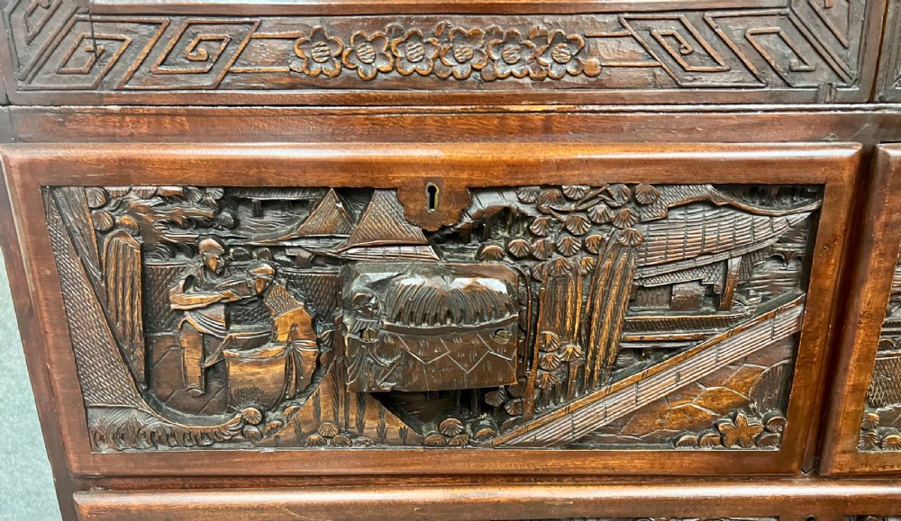 Intricately relief-carved dark camphor wood cabinet-on-chest featuring two upper cupboard doors decorated with figurative scenes above two short and one long drawer. View VI