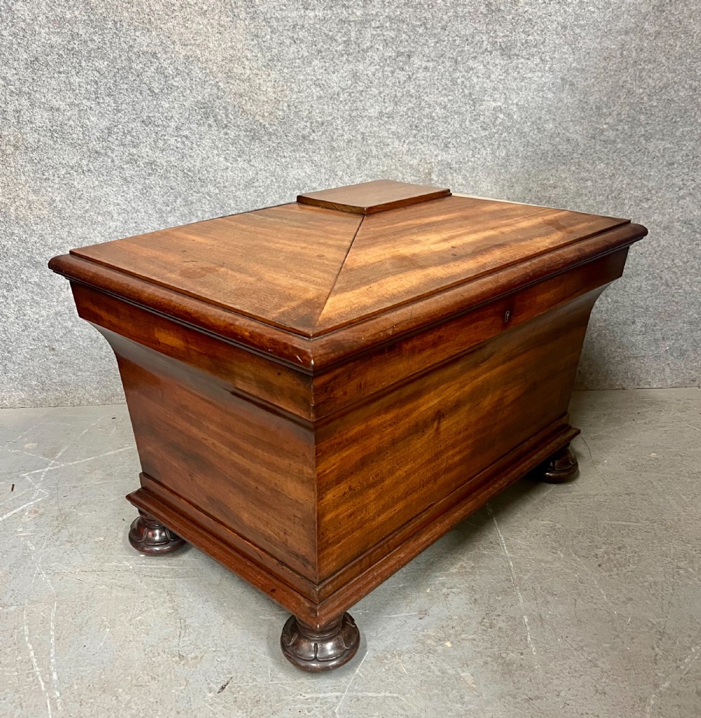 A sarcophagus-shaped antique mahogany wine cellarette with a flared lid, tapered sides, and carved turned feet.