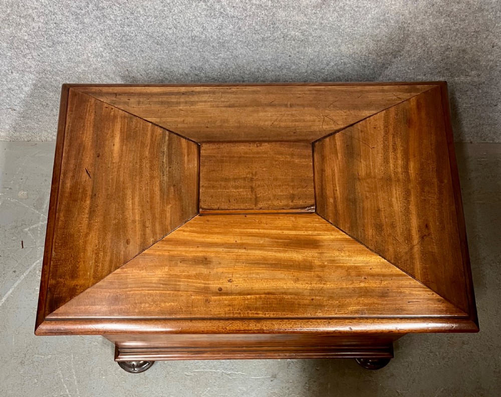 A sarcophagus-shaped antique mahogany wine cellarette with a flared lid, tapered sides, and carved turned feet. View VII