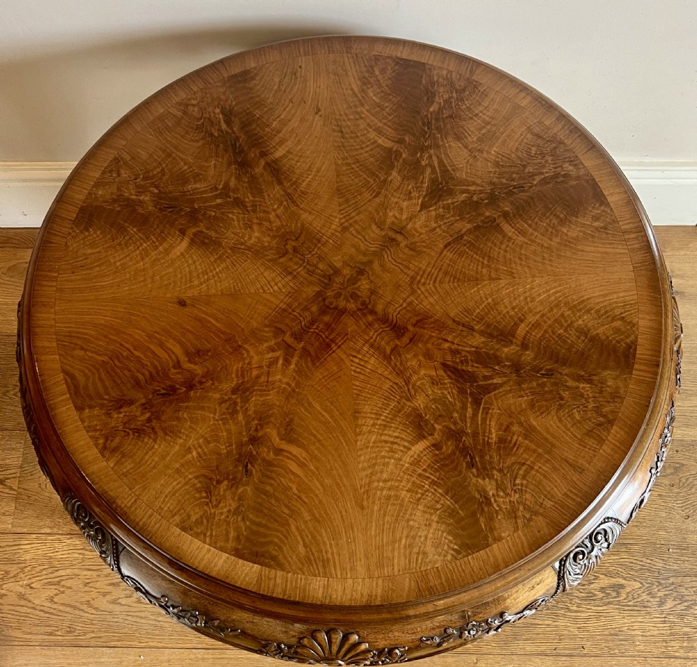 A circular walnut coffee table featuring a quartered figured walnut top, a deeply carved apron with floral motifs, and carved cabriole legs. View II