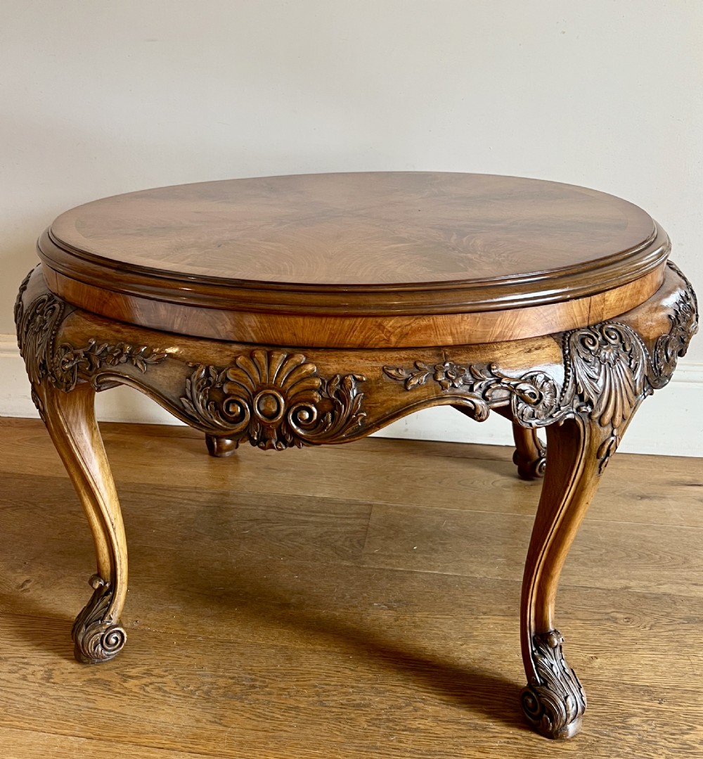 A circular walnut coffee table featuring a quartered figured walnut top, a deeply carved apron with floral motifs, and carved cabriole legs. View III