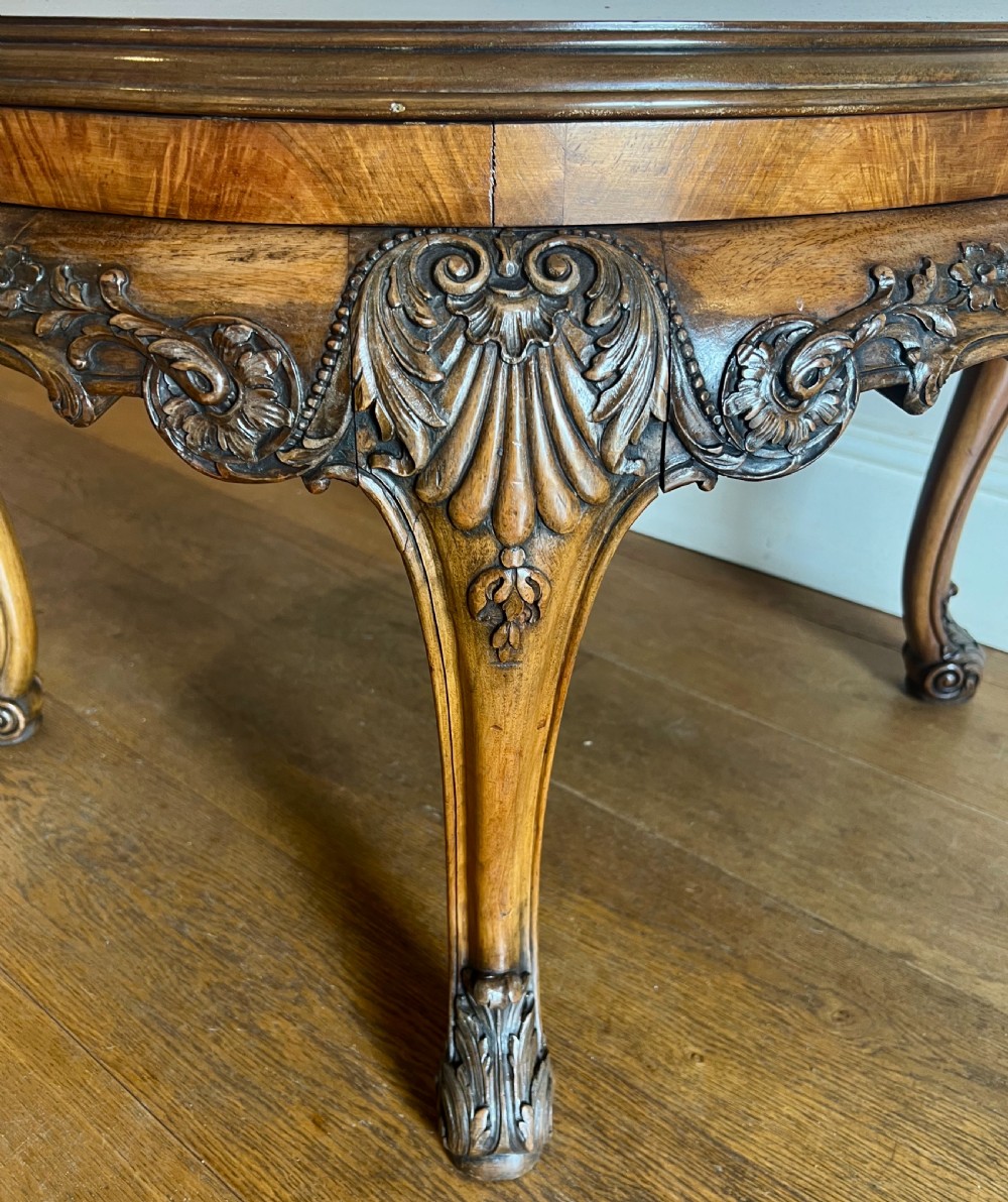 A circular walnut coffee table featuring a quartered figured walnut top, a deeply carved apron with floral motifs, and carved cabriole legs. View IV