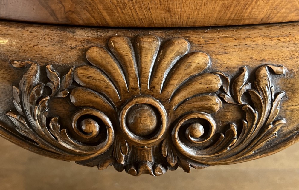 A circular walnut coffee table featuring a quartered figured walnut top, a deeply carved apron with floral motifs, and carved cabriole legs. View V