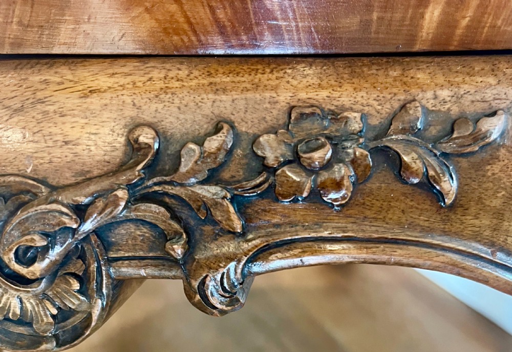 A circular walnut coffee table featuring a quartered figured walnut top, a deeply carved apron with floral motifs, and carved cabriole legs. View VI