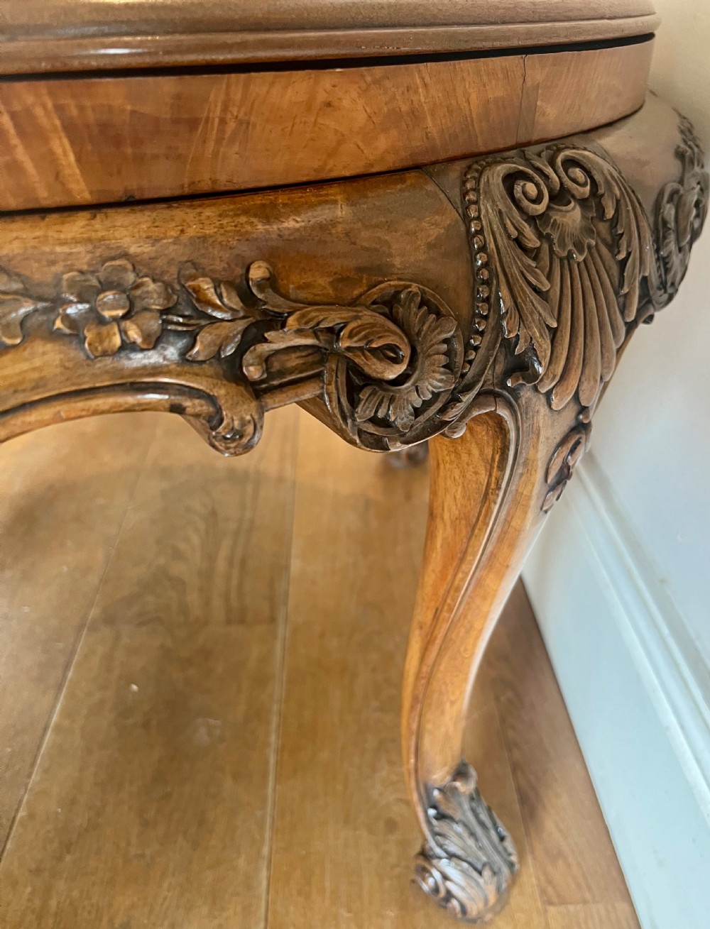 A circular walnut coffee table featuring a quartered figured walnut top, a deeply carved apron with floral motifs, and carved cabriole legs. View VII