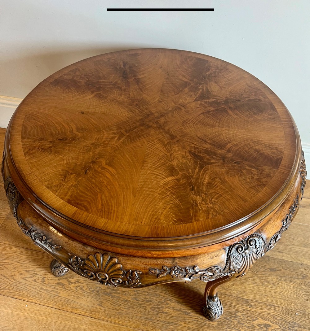 A circular walnut coffee table featuring a quartered figured walnut top, a deeply carved apron with floral motifs, and carved cabriole legs. View VIII