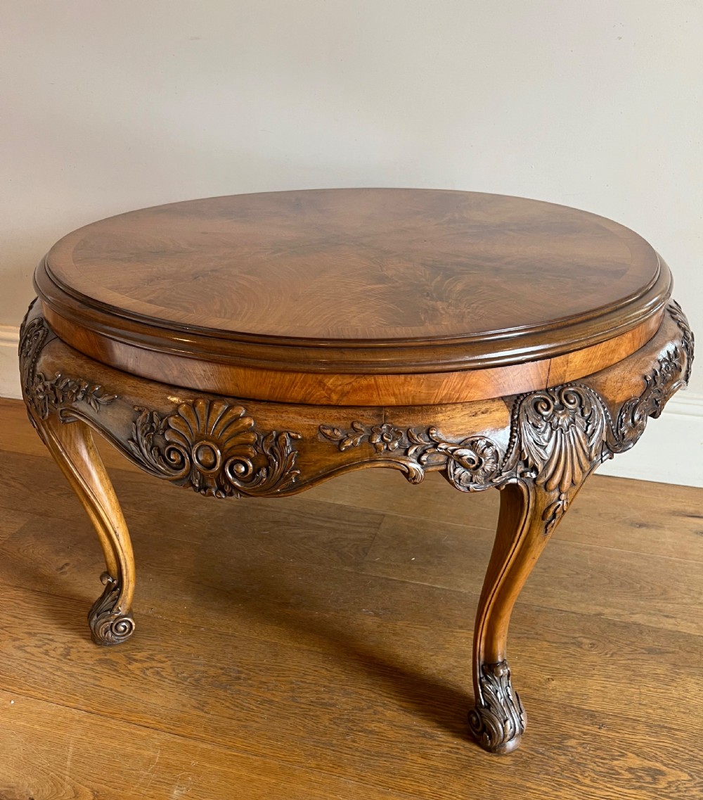A circular walnut coffee table featuring a quartered figured walnut top, a deeply carved apron with floral motifs, and carved cabriole legs. View IX