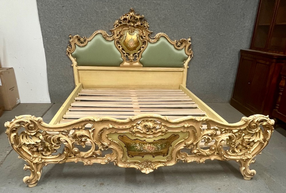 An ornate French Rococo style king size bed frame featuring cream painted and carved wood with gilded accents, sage green upholstered headboard panels, and hand-painted floral cartouches. View X