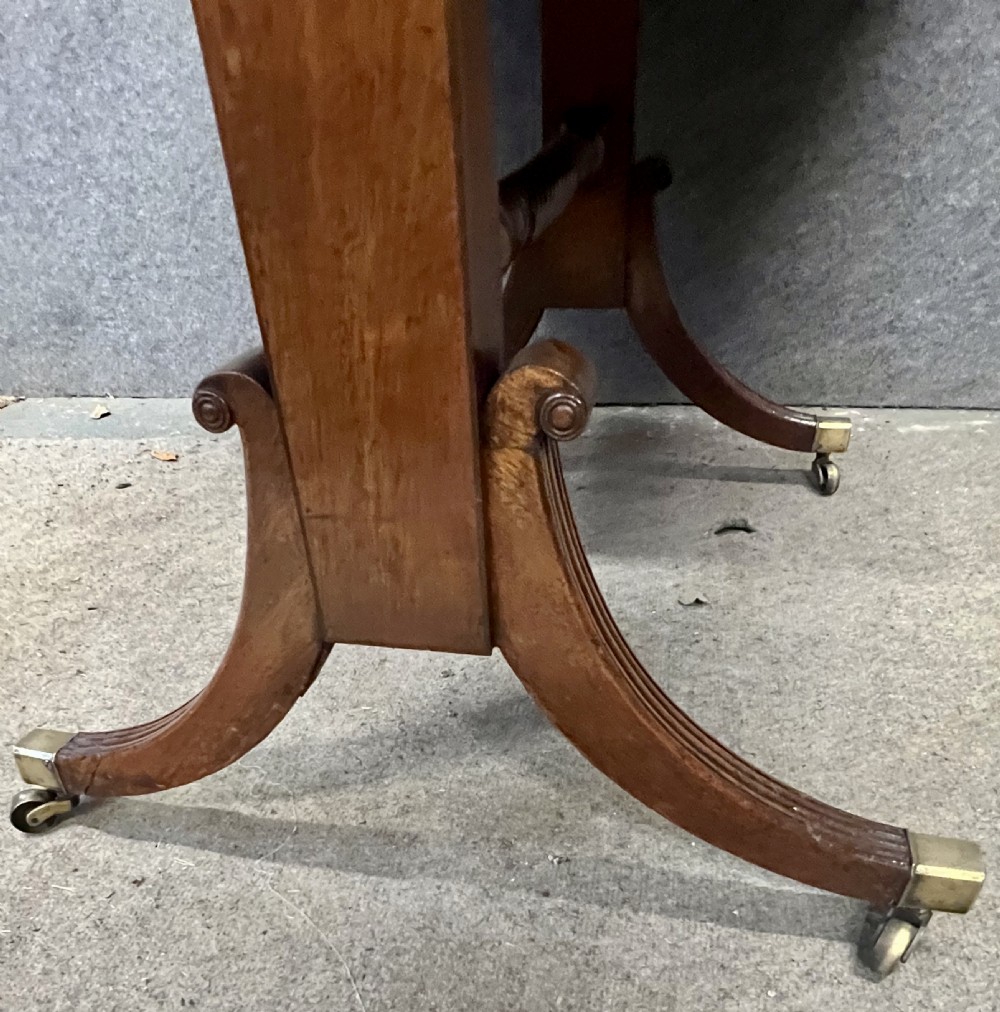 An antique Regency mahogany sofa table featuring two hinged drop leaves, a reeded timber border, twin reeded sabre legs joined by a turned stretcher, and brass caps on castors. View VIII