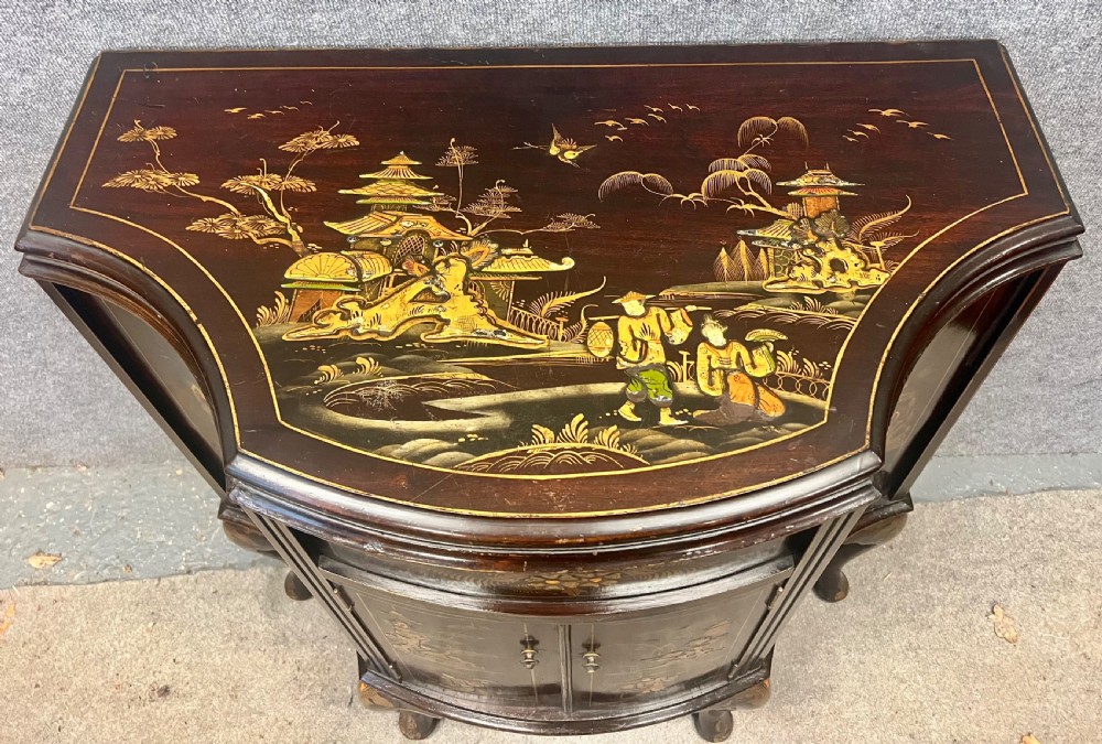 A dark lacquered bow-front Chinoiserie cabinet featuring gilded pictorial landscapes and cabriole legs. View III