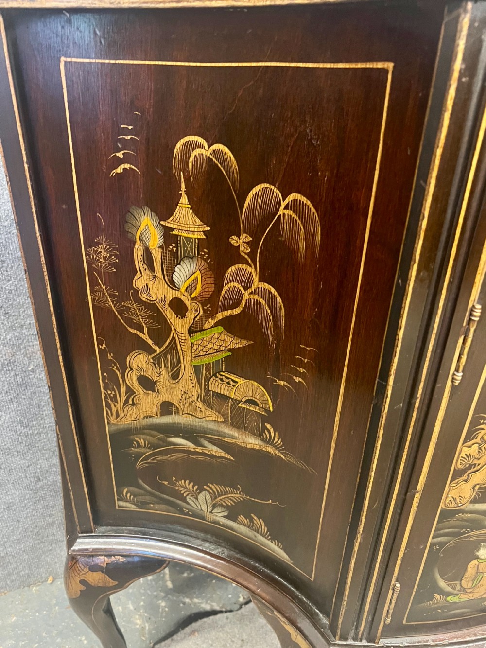 A dark lacquered bow-front Chinoiserie cabinet featuring gilded pictorial landscapes and cabriole legs. View IV