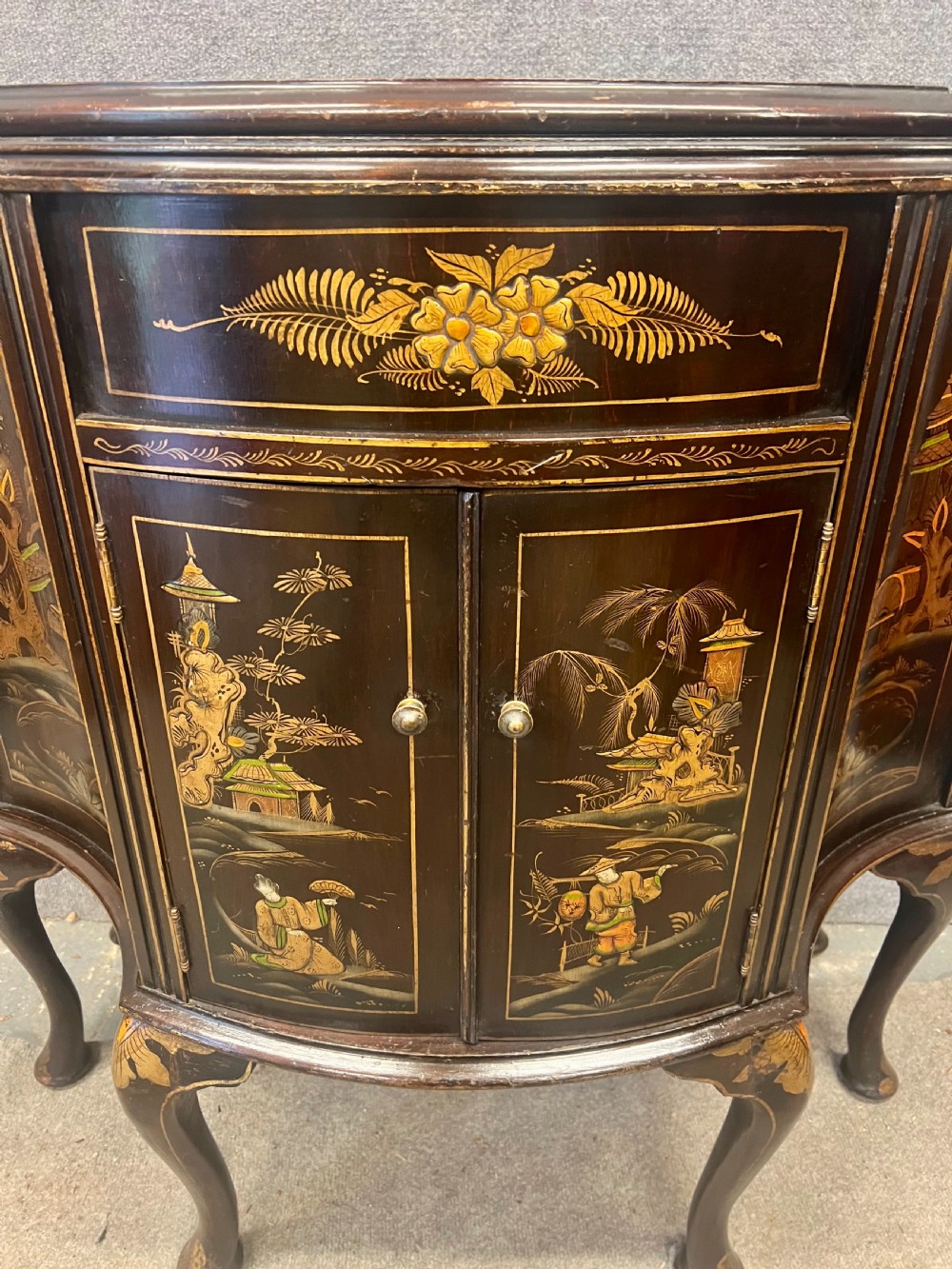 A dark lacquered bow-front Chinoiserie cabinet featuring gilded pictorial landscapes and cabriole legs. View V