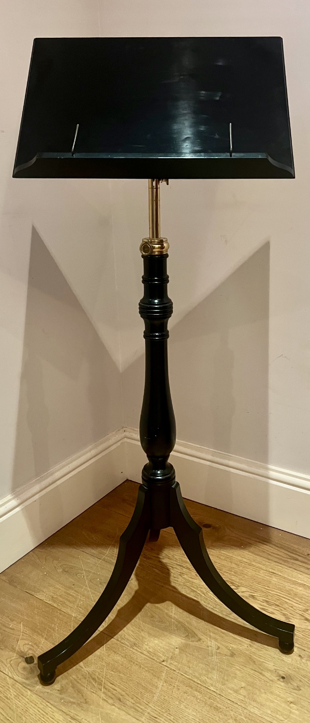 An ebonised wooden reading stand featuring a flat adjustable rest with brass page retainers, mounted on a turned column with a brass height adjustment fitting and a tripod base.