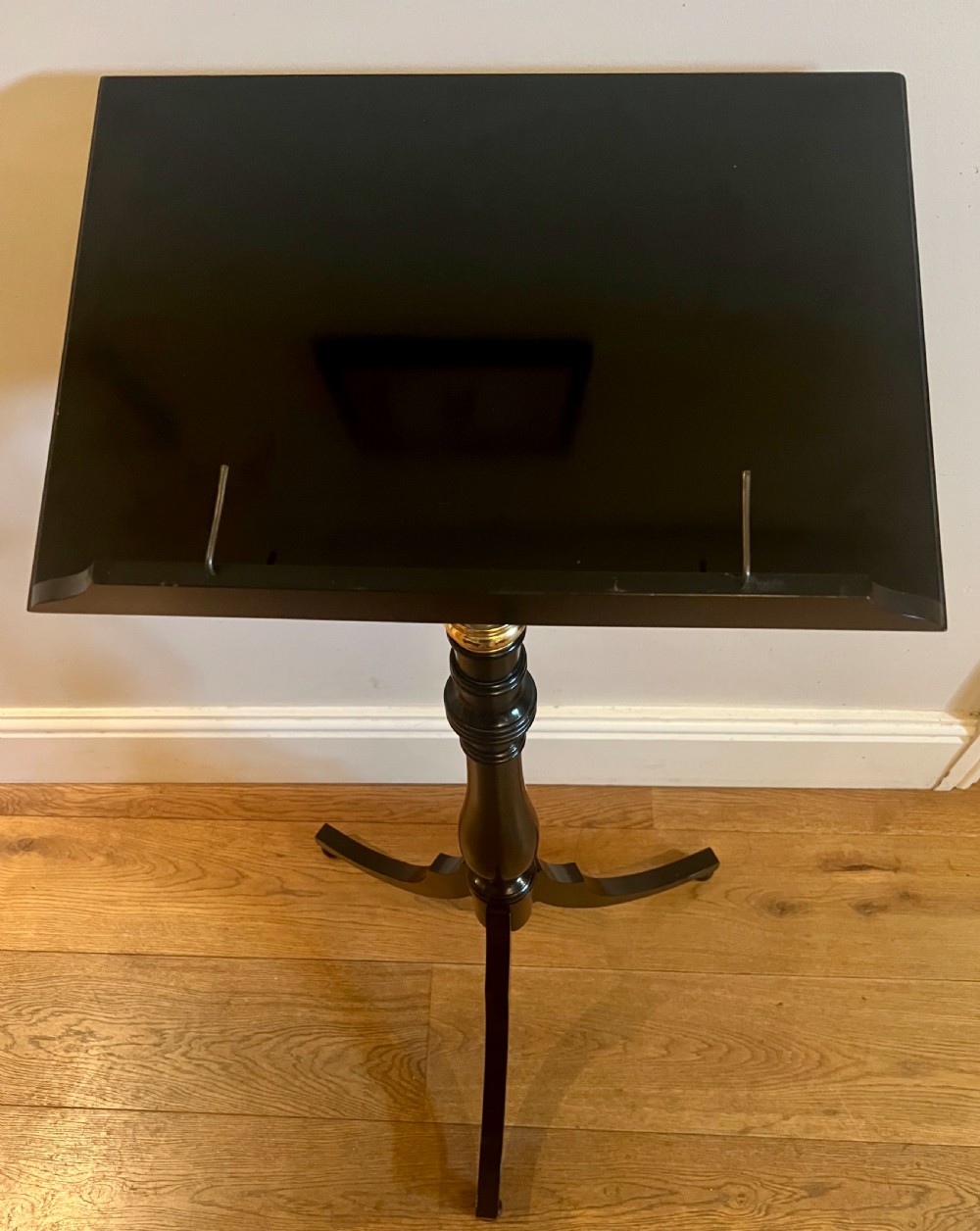 An ebonised wooden reading stand featuring a flat adjustable rest with brass page retainers, mounted on a turned column with a brass height adjustment fitting and a tripod base. View V