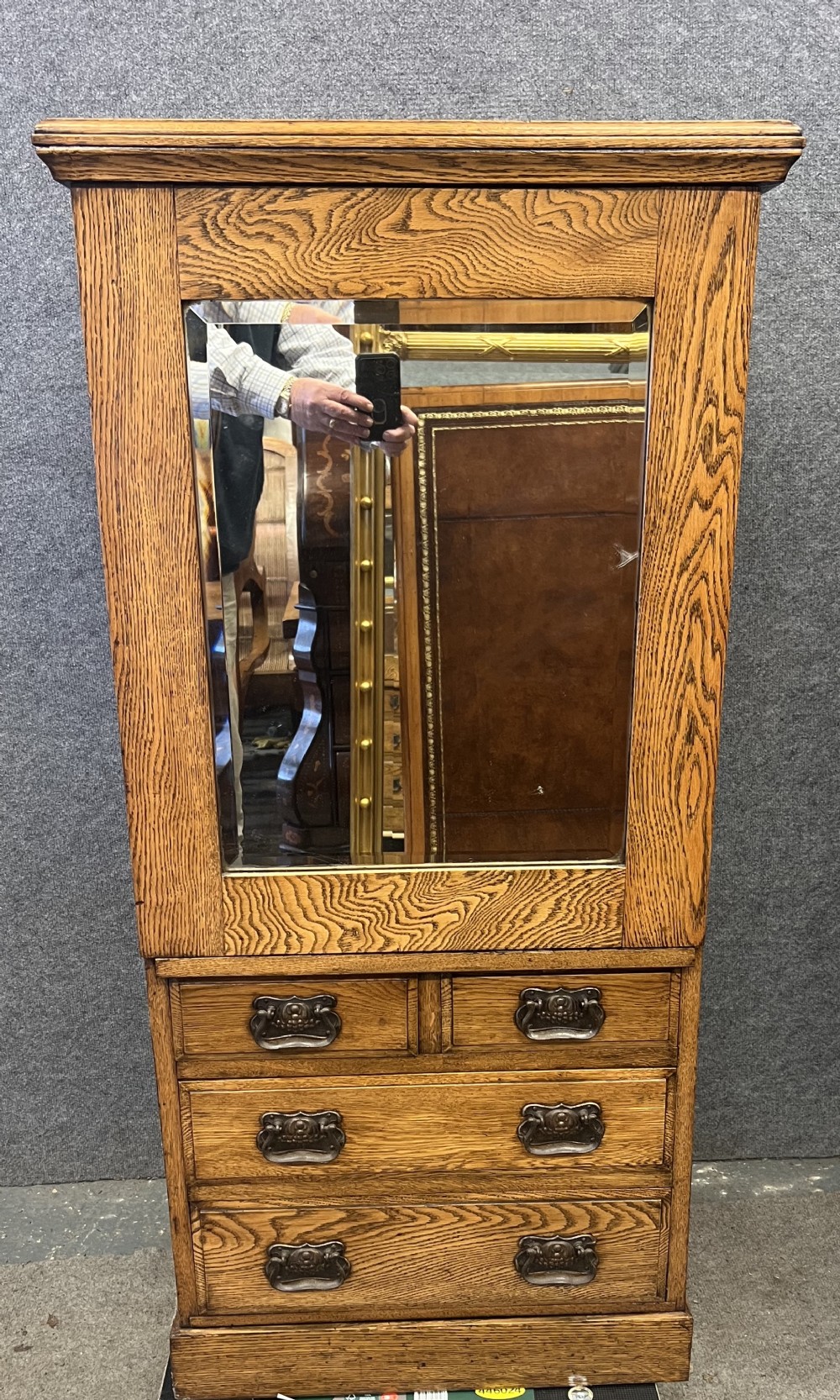 A tall Edwardian golden oak safe cabinet featuring a mirrored upper door panel, pronounced wood grain, and four drawers with metal bail handles.