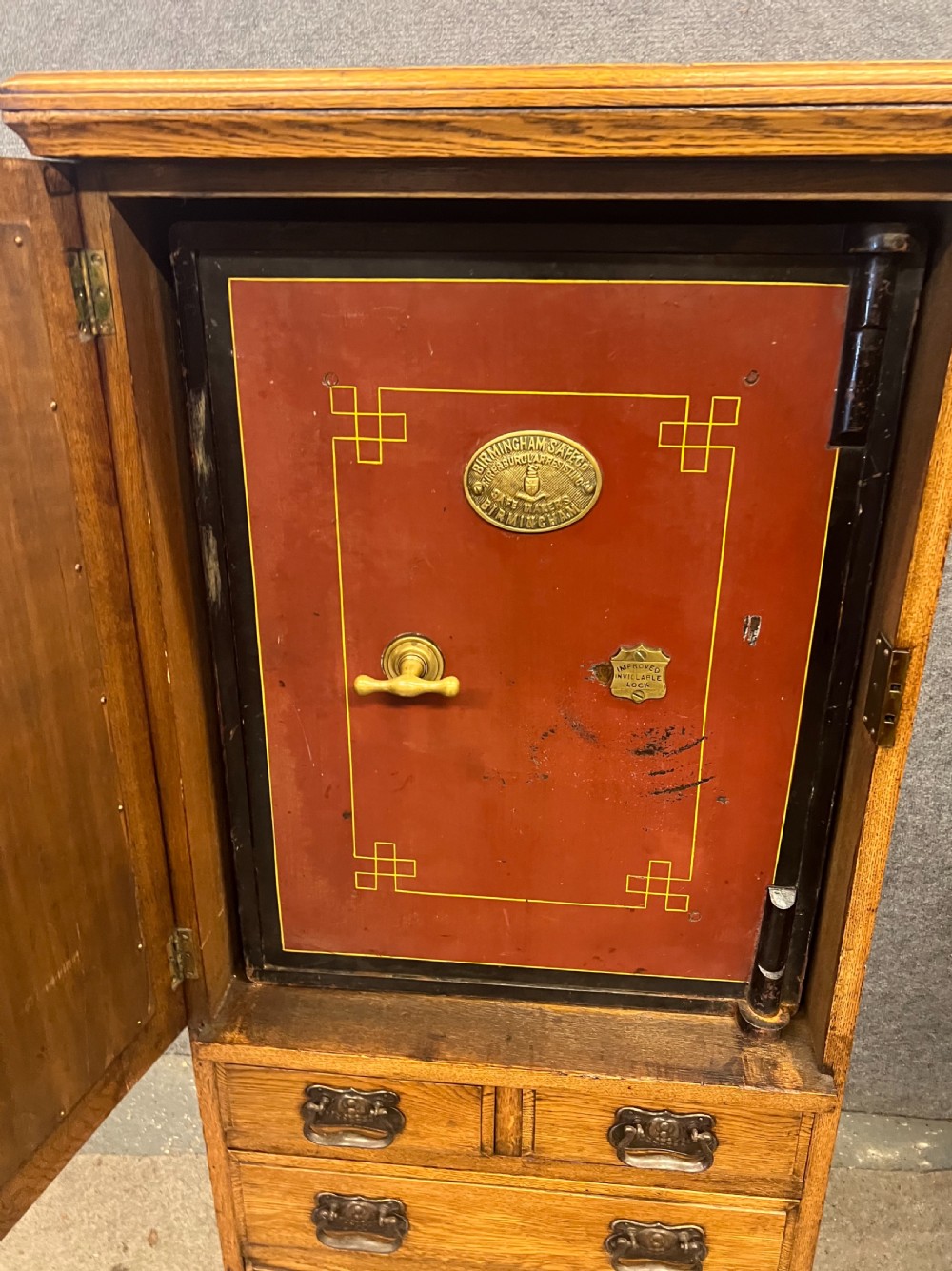 A tall Edwardian golden oak safe cabinet featuring a mirrored upper door panel, pronounced wood grain, and four drawers with metal bail handles. View II