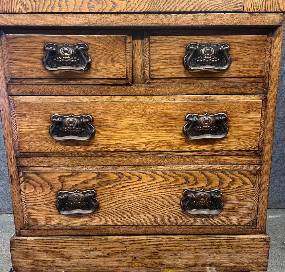 A tall Edwardian golden oak safe cabinet featuring a mirrored upper door panel, pronounced wood grain, and four drawers with metal bail handles. View III