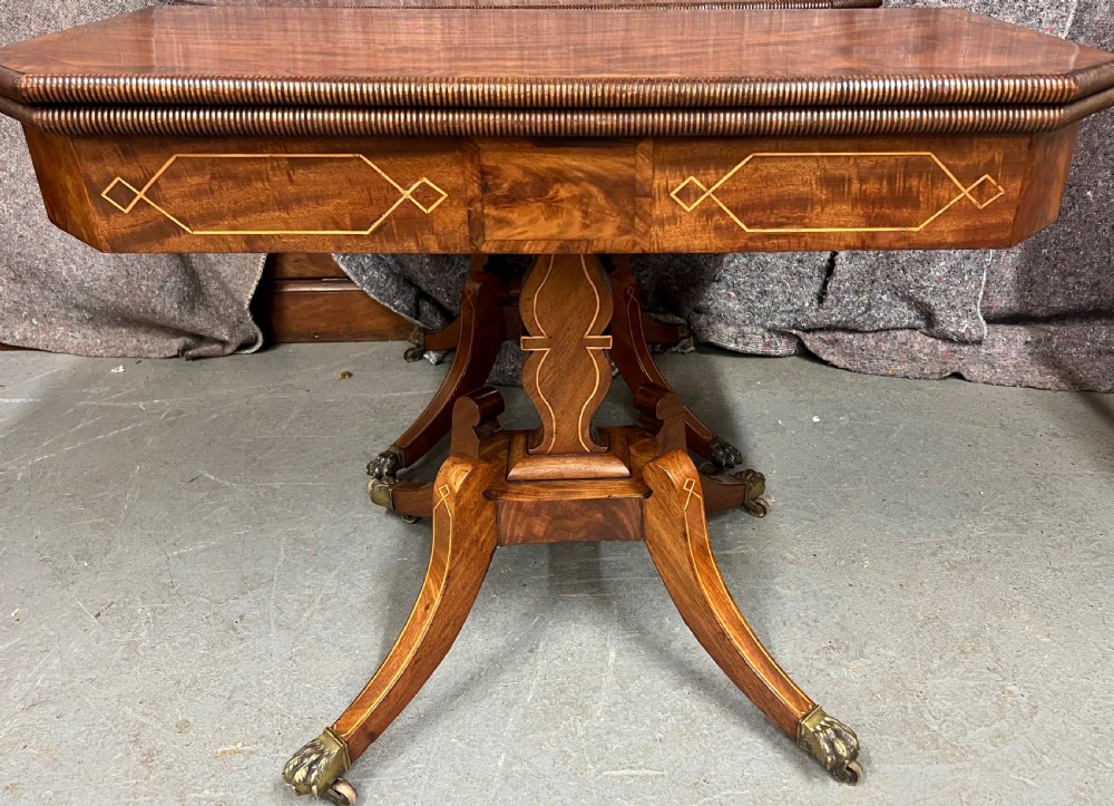 A pair of Regency flame mahogany fold-over card tables featuring boxwood inlay, reeded edges, and pedestal bases with splayed legs ending in brass paw castors. View IV