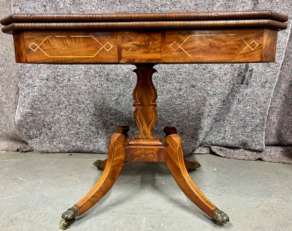 A pair of Regency flame mahogany fold-over card tables featuring boxwood inlay, reeded edges, and pedestal bases with splayed legs ending in brass paw castors. View V