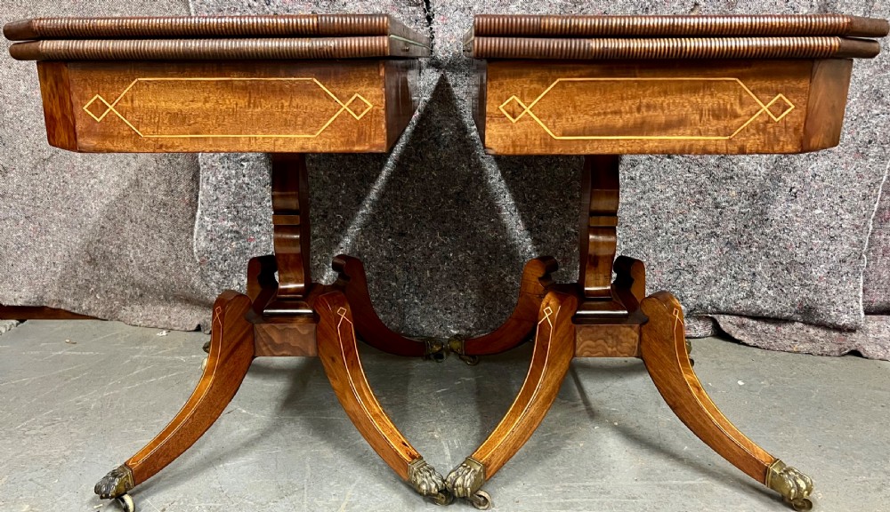 A pair of Regency flame mahogany fold-over card tables featuring boxwood inlay, reeded edges, and pedestal bases with splayed legs ending in brass paw castors. View VI