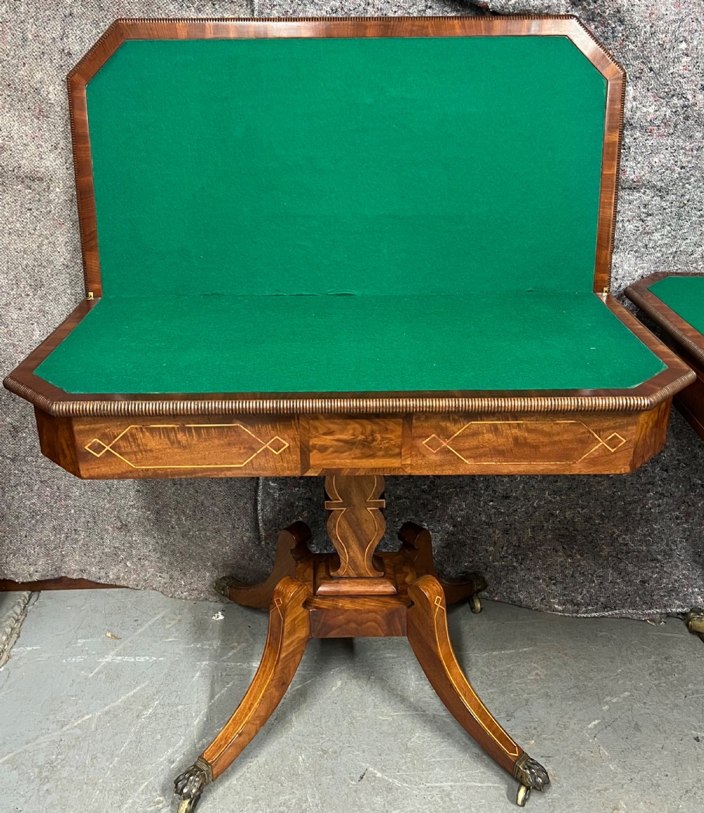 A pair of Regency flame mahogany fold-over card tables featuring boxwood inlay, reeded edges, and pedestal bases with splayed legs ending in brass paw castors. View VIII