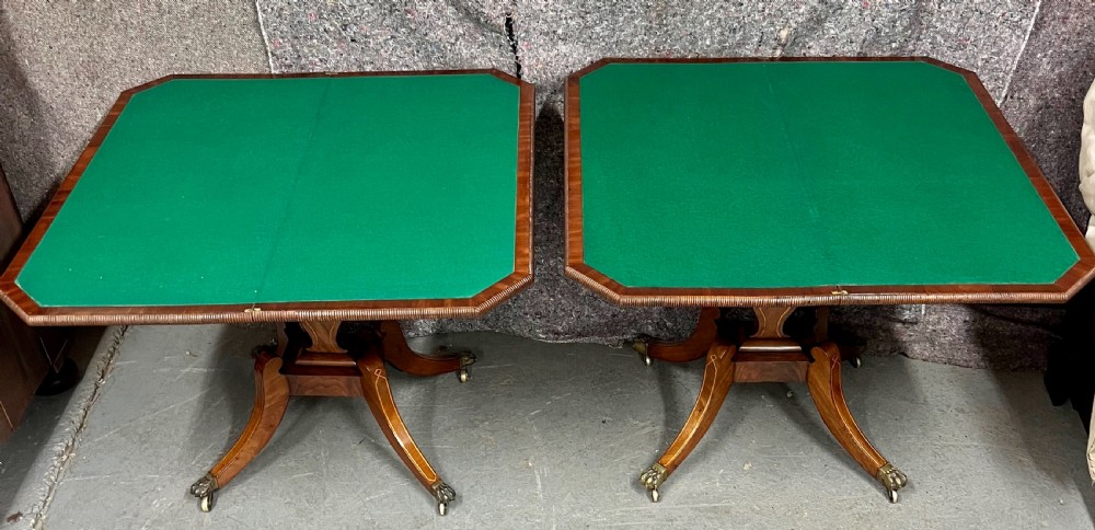 A pair of Regency flame mahogany fold-over card tables featuring boxwood inlay, reeded edges, and pedestal bases with splayed legs ending in brass paw castors. View IX