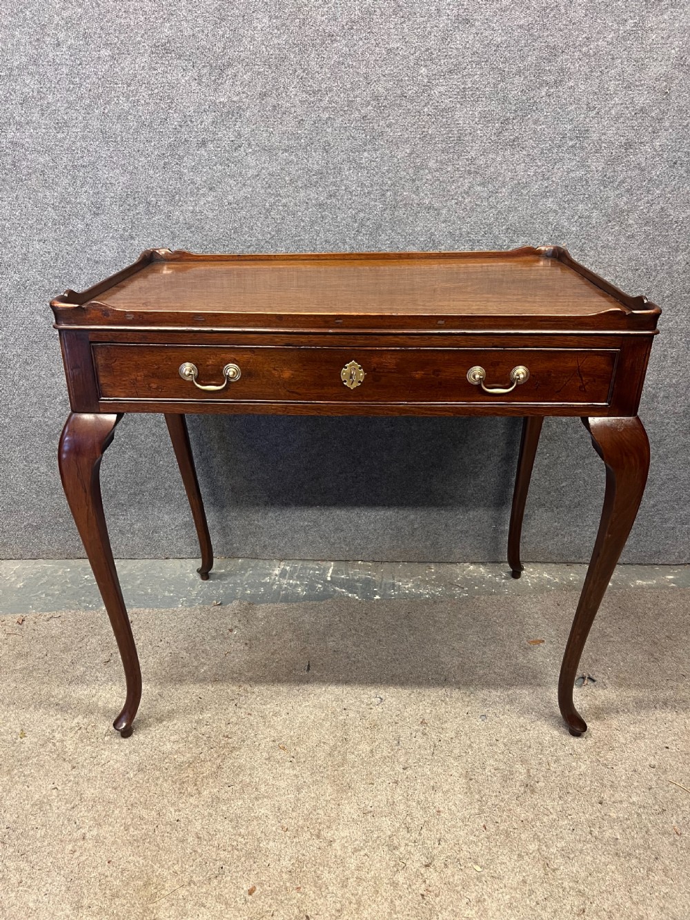 A Georgian mahogany silver table featuring a raised gallery top, a single drawer with brass handles, and slender cabriole legs.