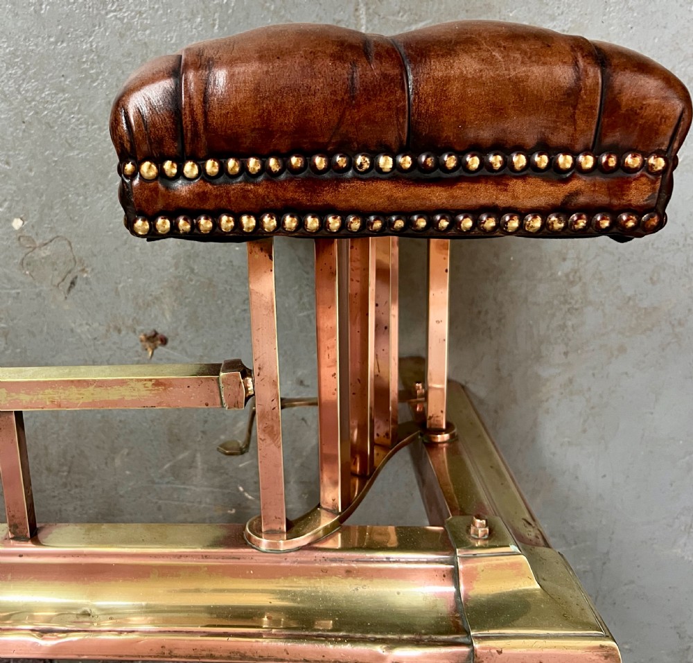An antique brass and copper club fender featuring two button-tufted brown leather corner seats with brass stud detailing set on a low metal base. View IV