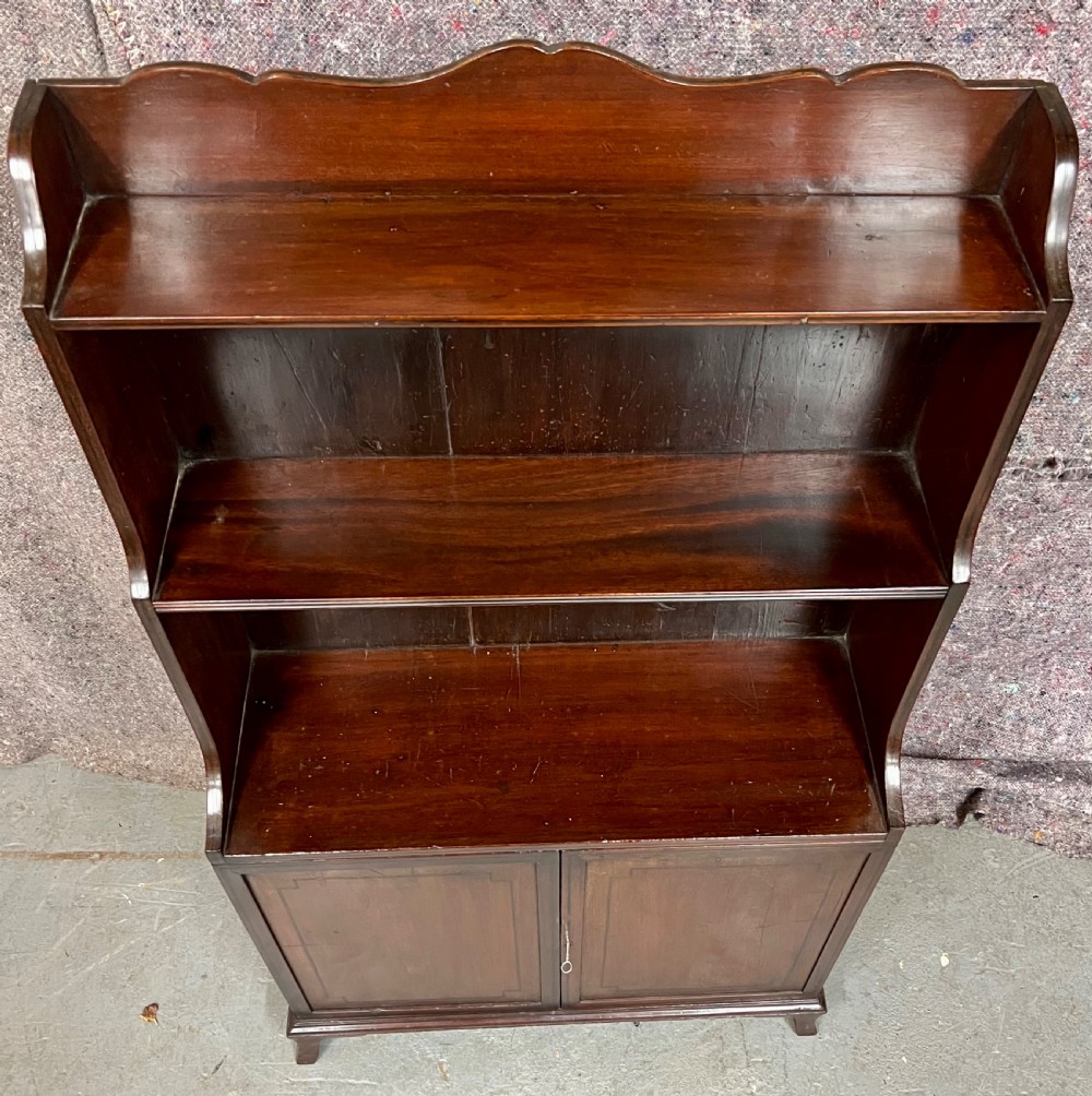 A George III mahogany waterfall bookcase featuring graduated open upper shelves above a panelled two-door cupboard base raised on bracket feet. View II