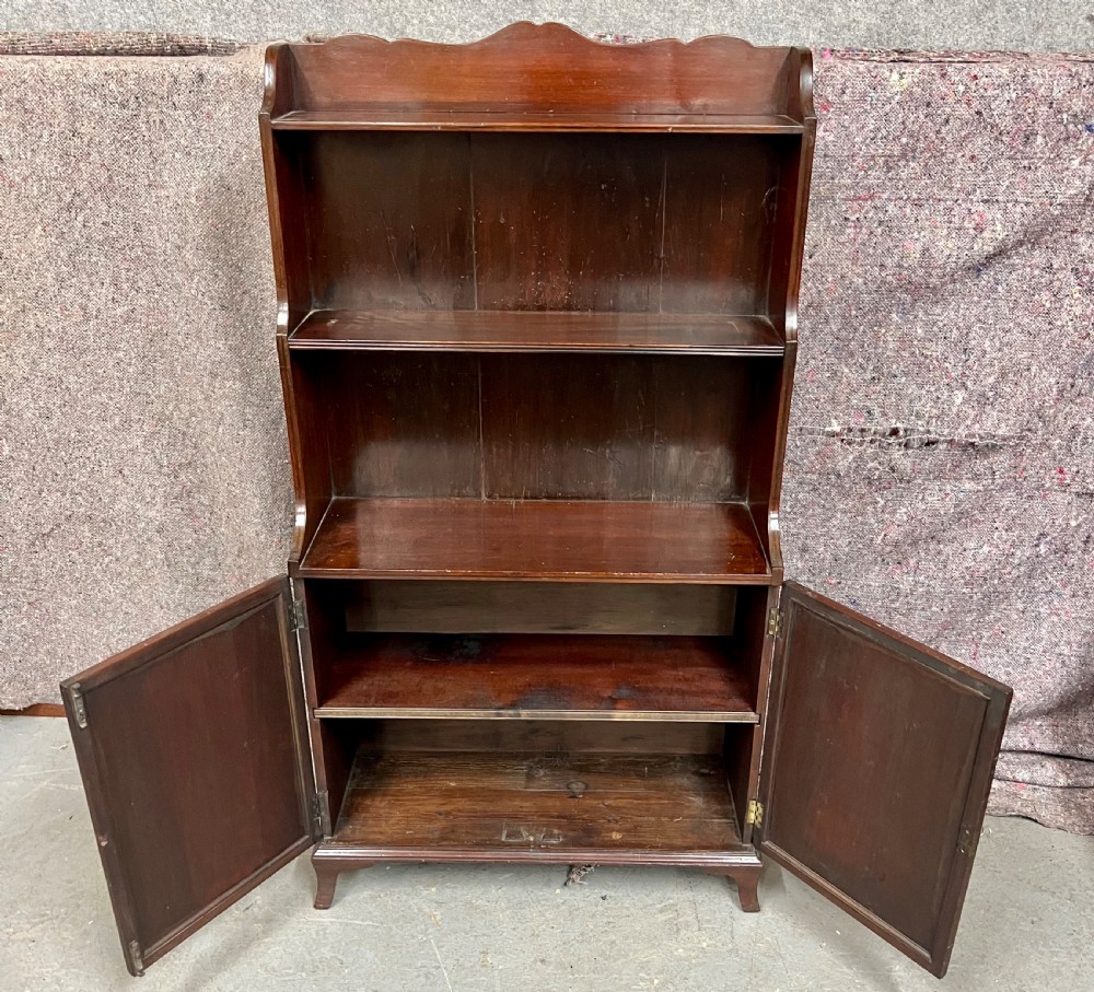 A George III mahogany waterfall bookcase featuring graduated open upper shelves above a panelled two-door cupboard base raised on bracket feet. View V