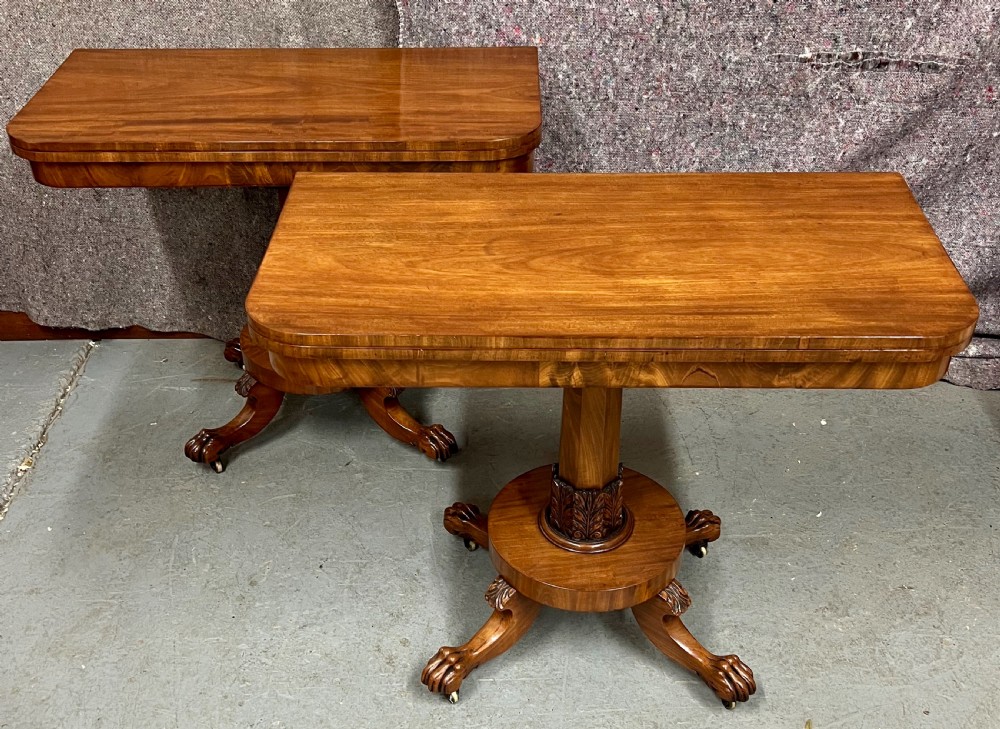 A pair of antique flame mahogany fold-over console tables featuring central carved pedestal columns and claw feet with castors.