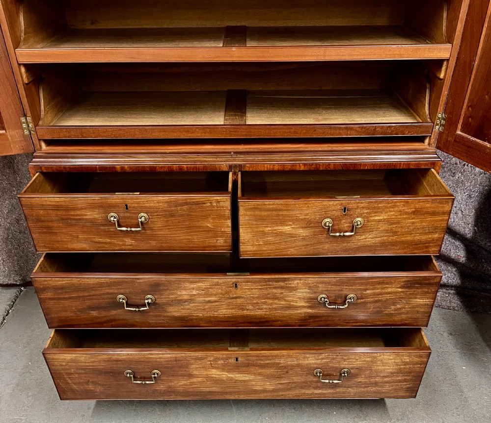 A George IV mahogany linen press featuring an arched pediment with oval inlay, double doors with oval flame mahogany panels, and a chest of drawers base. View V