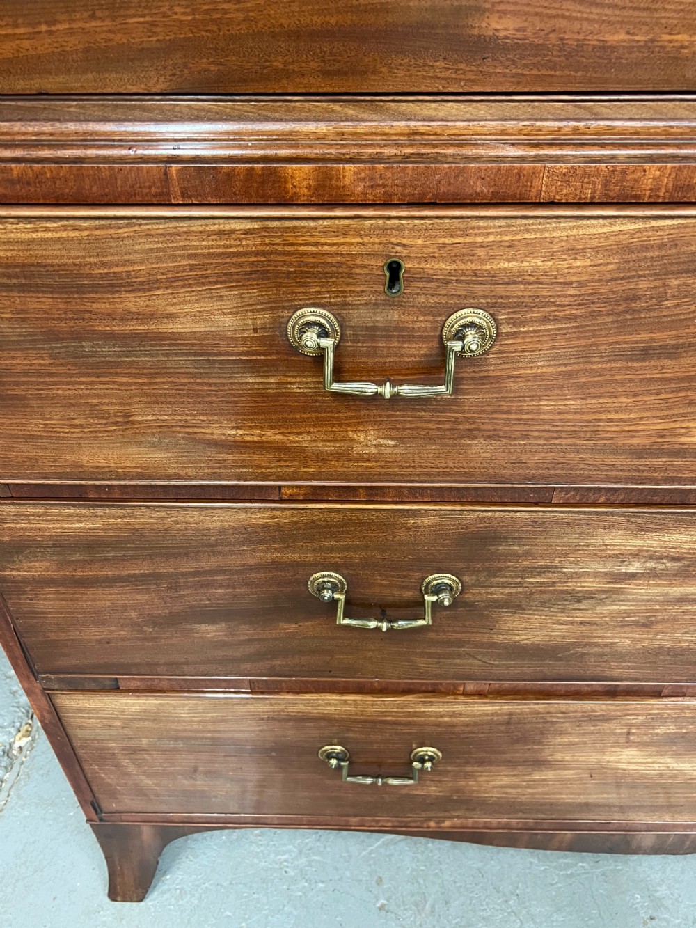 A George IV mahogany linen press featuring an arched pediment with oval inlay, double doors with oval flame mahogany panels, and a chest of drawers base. View VI