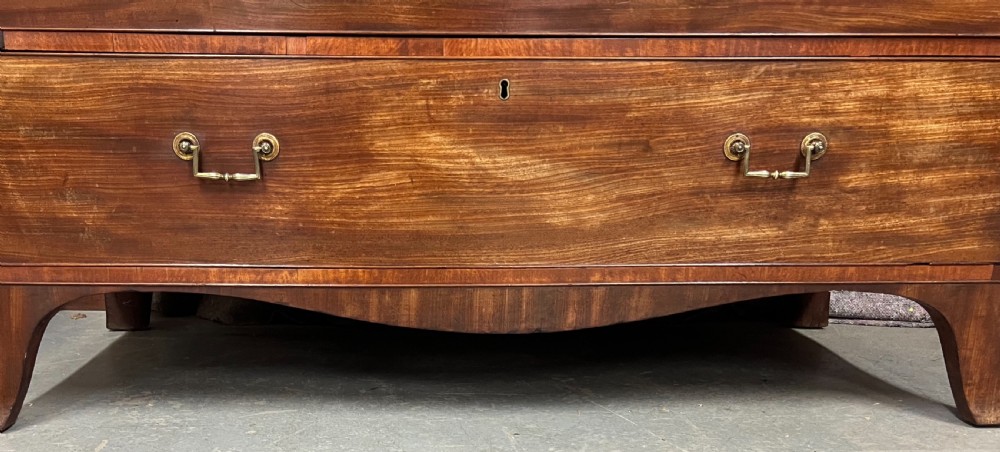 A George IV mahogany linen press featuring an arched pediment with oval inlay, double doors with oval flame mahogany panels, and a chest of drawers base. View VII