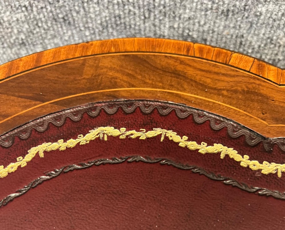 An Edwardian kidney-shaped mahogany writing table featuring a deep red leather insert with gilt tooling, satinwood string inlay, turned fluted legs, brass castors, and a central curved drawer. View II