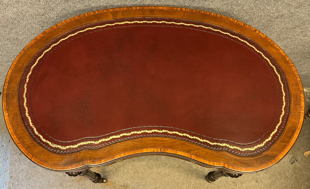 An Edwardian kidney-shaped mahogany writing table featuring a deep red leather insert with gilt tooling, satinwood string inlay, turned fluted legs, brass castors, and a central curved drawer. View VIII