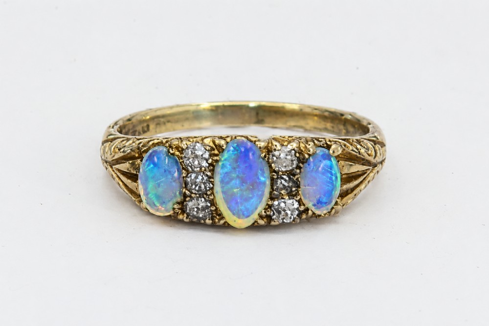 An antique 18ct yellow gold ring set with three oval opals and four accent diamonds featuring carved scroll shoulders.