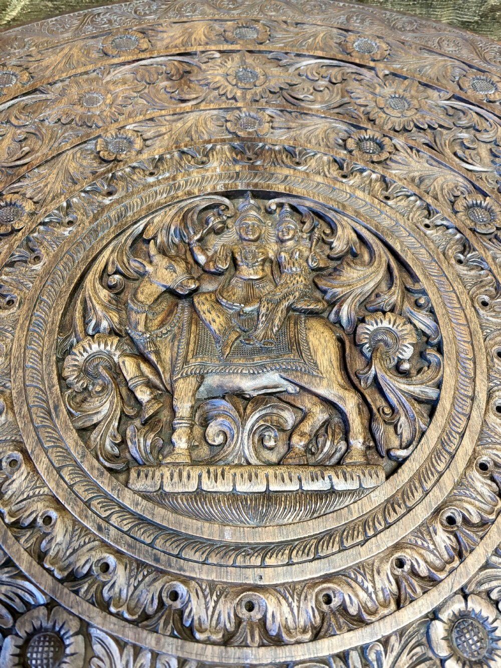 A large circular dark teak Anglo-Indian table featuring a deeply hand-carved floral top supported by three carved elephant legs with white tusks. View III